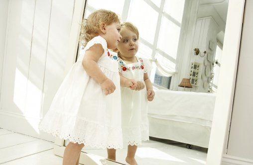 Baby girl (18-24 months) looking in mirror, side view